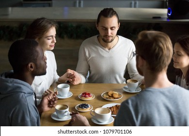 Grateful multiracial young friends holding hands sitting at home or cafeteria table saying grace concept, religious people blessing food praying meditating thanking before eating breakfast together - Powered by Shutterstock