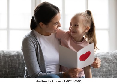 Grateful Young Woman Cuddling Smiling Pretty Little Kid Girl, Reading Wishes In Handmade Post Card, Celebrating International Women's Day Or Birthday, Close Sweet Tender Relationship Concept.