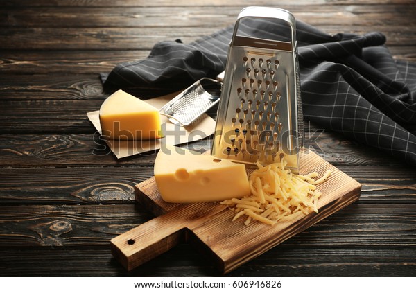 Grater and cheese on wooden\
board