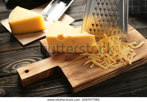 Grater and cheese on wooden\
board