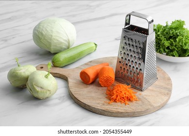 Grater and fresh vegetables on white marble table