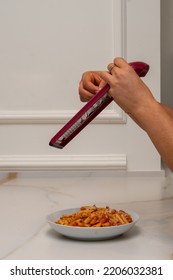 A Grater Is Held By The Hands Of A Woman, While Grating Cheese And Pouring It Onto A Plate Of Macaroni With Bolognese Sauce On A Marble Table And A Wall With Molding. Blurry Movement