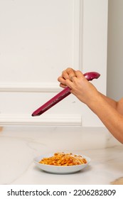 A Grater Is Held By The Hands Of A Woman, While Grating Cheese And Pouring It Onto A Plate Of Macaroni With Bolognese Sauce On A Marble Table And A Wall With Molding. Blurry Movement