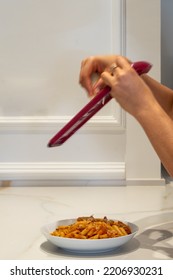 A Grater Is Held By The Hands Of A Woman, While Grating Cheese And Pouring It Onto A Plate Of Macaroni With Bolognese Sauce On A Marble Table And A Wall With Molding. Blurry Movement