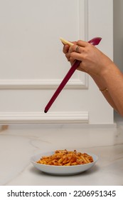 A Grater Is Held By The Hands Of A Woman, While Grating Cheese And Pouring It Onto A Plate Of Macaroni With Bolognese Sauce On A Marble Table And A Wall With Molding In The Background