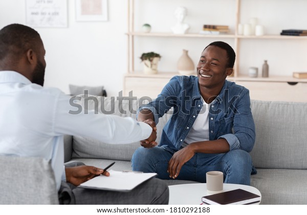 Gratittude For Work. Black Man Handshaking With
Psychologist After Therapy Session Meeting, Sitting On Couch At His
Office