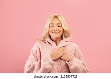 Gratitude concept. Thankful lady keeping both palms on chest and smiling with closed eyes, woman expressing appreciation and kindness while standing over pink background, free space