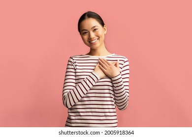 Gratitude Concept. Thankful Young Asian Woman Keeping Both Palms On Chest, Smiling Korean Female Expressing Appreciation And Kindness While Standing Isolated Over Pink Background, Copy Space
