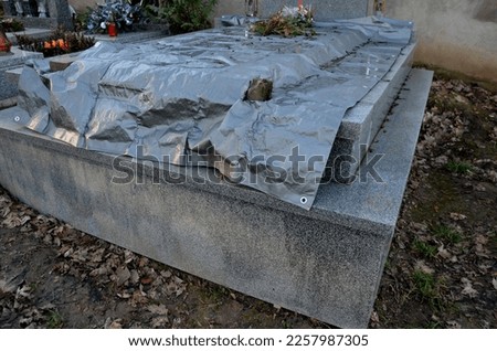 A grave covered with a gray tarpaulin is being renovated, or the stone slab is being replaced. exhumation of the dead for expert examination of the remains. suspicion of murder, poisoning