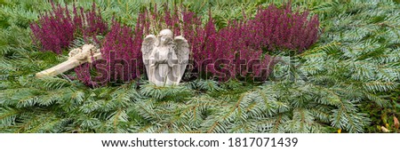 Grave decoration with an angel and a cross, fir branches and winter flowering heather, banner