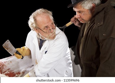 Grave Robber And Evil Doctor With Bloody Cleaver Exchange Glances. Stage Effect, Isolated On Black Background, Spot Lighting.