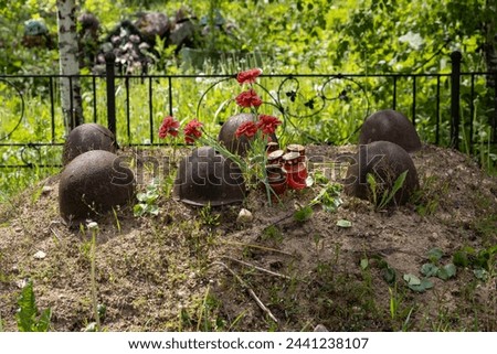 The grave of Soviet soldiers who died during the Great Patriotic War. Rusty helmets, candles and flowers on the grave. Memorial military cemetery in the village of Isakovo, Novgorod region, Russia.