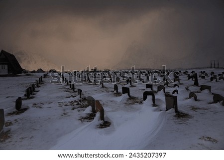 A grave yarad in winter with tomb stones buried in snow and a church at the background under mysterous cloudy sky