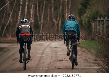 Gravel bike riding in rainy weather. Bikerider from behind wearing a safety helmet. Modern bicycle.
