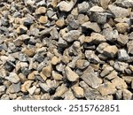 Gravel and crushed river stones illuminated by sunlight, arranged in a large pile. Used for road construction and repair projects, displaying rough textures and diverse sizes.