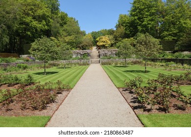 A gravel path runs between two verdant lawns before rising up several flights of steps and terraced gardens in the formal gardens of an English country house on the edge of Dartmoor National park