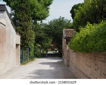 Gravel Road Between Brick Buildings Leading To A Garden House. Closed Gate.