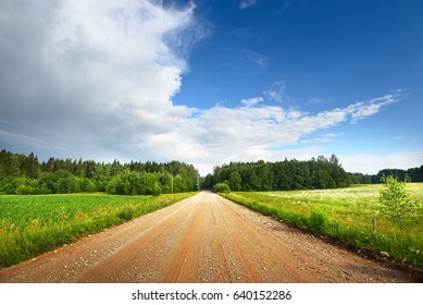 Gravel road going through field and forest in Latvia countryside