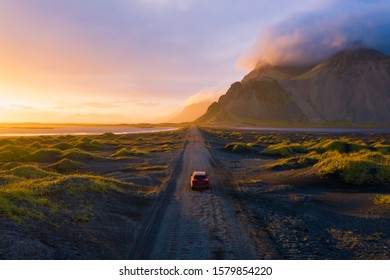 Gravel road at a golden Sunset with Vestrahorn mountain in the background and a car driving the road in Iceland