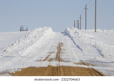 Gravel road lined with deep snow drifts.