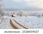 Gravel road in a rural winter landscape with hoarfrost and a red barn