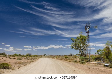 Gravel road and water pump windmill in outback town on cloudy day