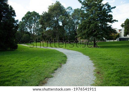 Gravel Walking track through grassy park in Glen Iris, Victoria Australia. Part of Ferndale Trail Ashburton. Textured green grass and trees and grainy gravel.