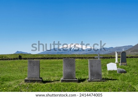 Gravestone on grass in Christian church cemetery and volcanic mountain on background in summer at Iceland