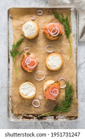 Gravlax A Raw, Marinated Graved Salmon With Dill On Bred Roll Bun With Cream Cheese, Onion Rings On Tray With Baking Paper And Light Marble Background