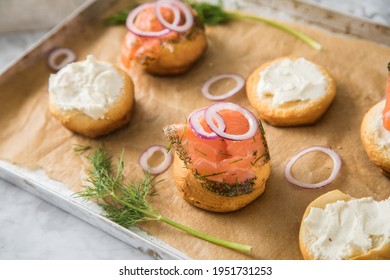 Gravlax A Raw, Marinated Graved Salmon With Dill On Bred Roll Bun With Cream Cheese, Onion Rings On Tray With Baking Paper And Light Marble Background