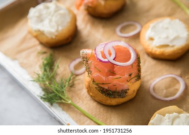 Gravlax A Raw, Marinated Graved Salmon With Dill On Bred Roll Bun With Cream Cheese, Onion Rings On Tray With Baking Paper And Light Marble Background