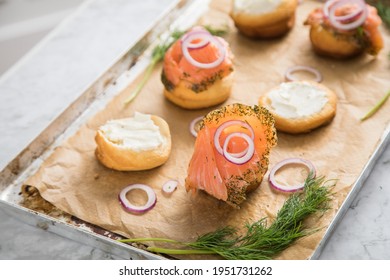 Gravlax A Raw, Marinated Graved Salmon With Dill On Bred Roll Bun With Cream Cheese, Onion Rings On Tray With Baking Paper And Light Marble Background