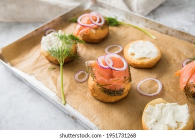 Gravlax A Raw, Marinated Graved Salmon With Dill On Bred Roll Bun With Cream Cheese, Onion Rings On Tray With Baking Paper And Light Marble Background