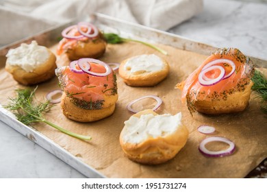 Gravlax A Raw, Marinated Graved Salmon With Dill On Bred Roll Bun With Cream Cheese, Onion Rings On Tray With Baking Paper And Light Marble Background