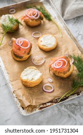 Gravlax A Raw, Marinated Graved Salmon With Dill On Bred Roll Bun With Cream Cheese, Onion Rings On Tray With Baking Paper And Light Marble Background