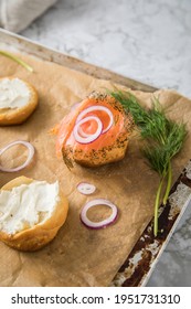 Gravlax A Raw, Marinated Graved Salmon With Dill On Bred Roll Bun With Cream Cheese, Onion Rings On Tray With Baking Paper And Light Marble Background