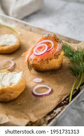 Gravlax A Raw, Marinated Graved Salmon With Dill On Bred Roll Bun With Cream Cheese, Onion Rings On Tray With Baking Paper And Light Marble Background