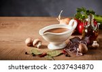 Gravy boat or pitcher with savory spicy gravy and fresh healthy assortment of vegetables, seasoning and olive oil on a wooden kitchen table with copyspace