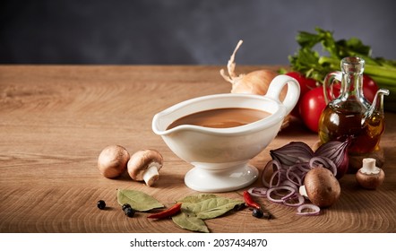 Gravy boat or pitcher with savory spicy gravy and fresh healthy assortment of vegetables, seasoning and olive oil on a wooden kitchen table with copyspace - Shutterstock ID 2037434870
