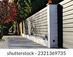 gray aluminum fence and gate. horizontal panels. narrow gaps.  powder coated finish. diminishing perspective view. modern fence design concept. concrete sidewalk. white stucco base and fence piers