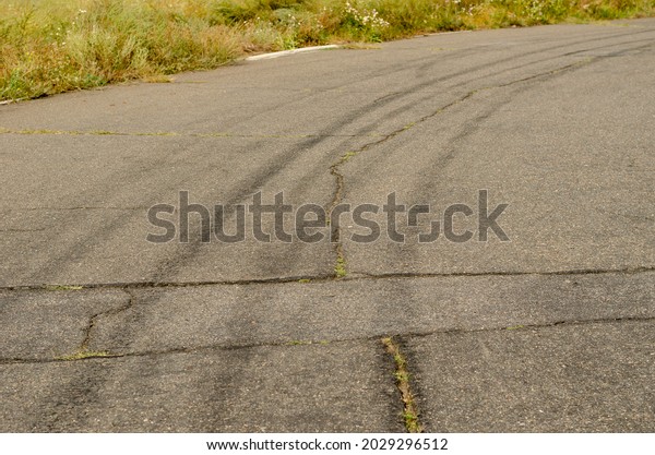 Gray asphalt with black tire\
tracks. An old country road with cracks. Green grass on the side of\
the highway. Curved wheel tracks in a bend in the\
driveway.