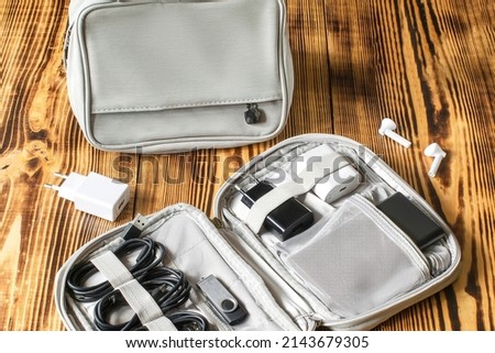 Gray bag, charger handbag, cables, flesh driver, power bank organizer for road trip, work vacation, business trip on wooden table.