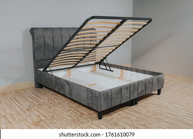 A gray bed with a storage space revealed by lifting the wooden slatted base