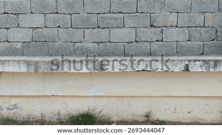 A gray brick wall with a concrete ledge and a painted base, showing signs of wear and tear near the ground.