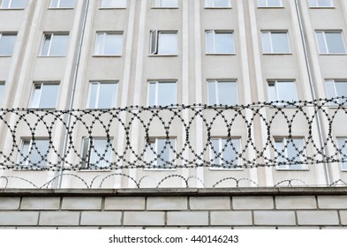 Gray Building Is Fenced With Barbed Wire. Symbol Of  Dictatorial And Authoritarian Regime. Limitation Limitation Of Freedom And Human Rights.