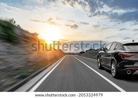 Gray car on a scenic road. Car on the road surrounded by a magnificent natural landscape in the rays of sunset or dawn.