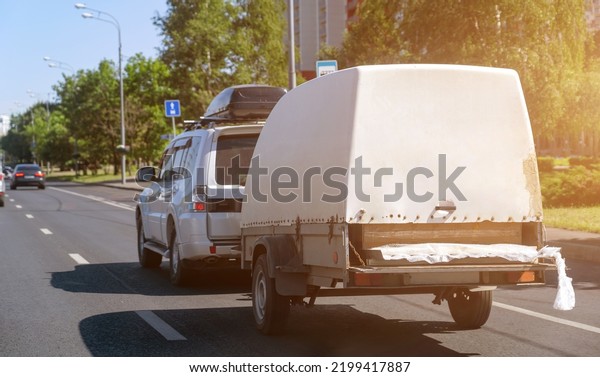 Gray car with roof rack and utility trailer on road\
at residential city area.
