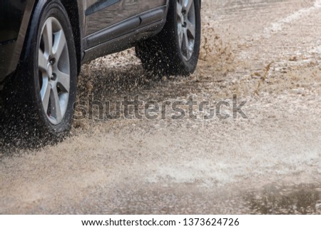 A gray car speeding through the sewage road splashing yellow water splash