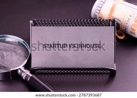 A gray card marked STARTUP VS INHOUSE rests in a black holder on a dark surface.