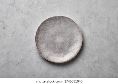 Gray Ceramic Plate On Grey Concrete Rough Background. Empty Spotted Uneven Saucer. Matte Dish On Stone Textured Backdrop. Hand Made Ceramic Table Setting. Top View